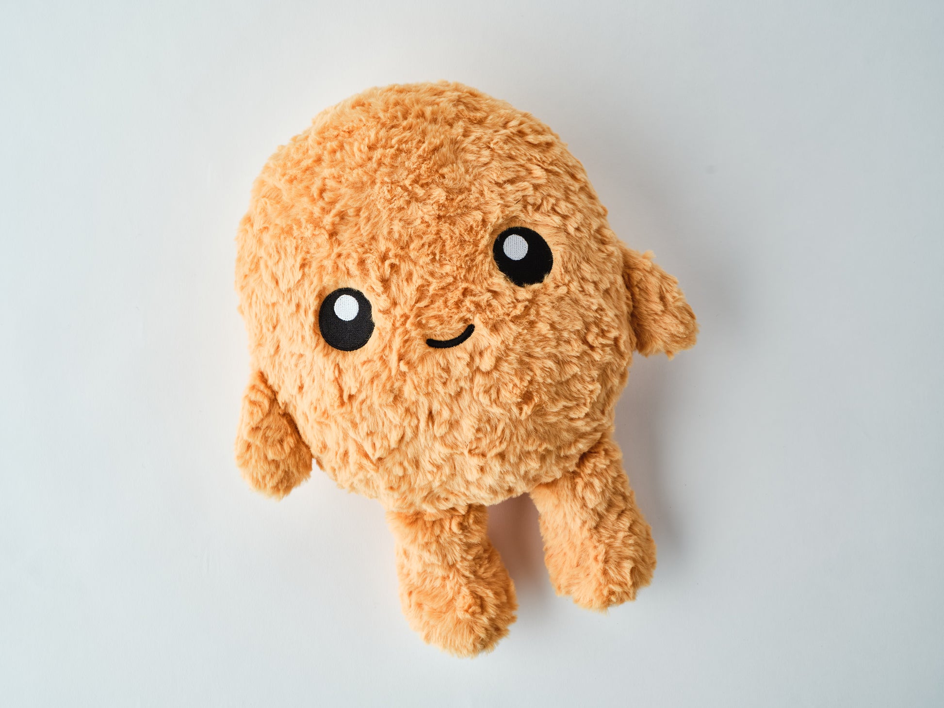 Adorable orange plush toy with fuzzy texture, small arms and legs, and a happy embroidered face lying on a white surface.